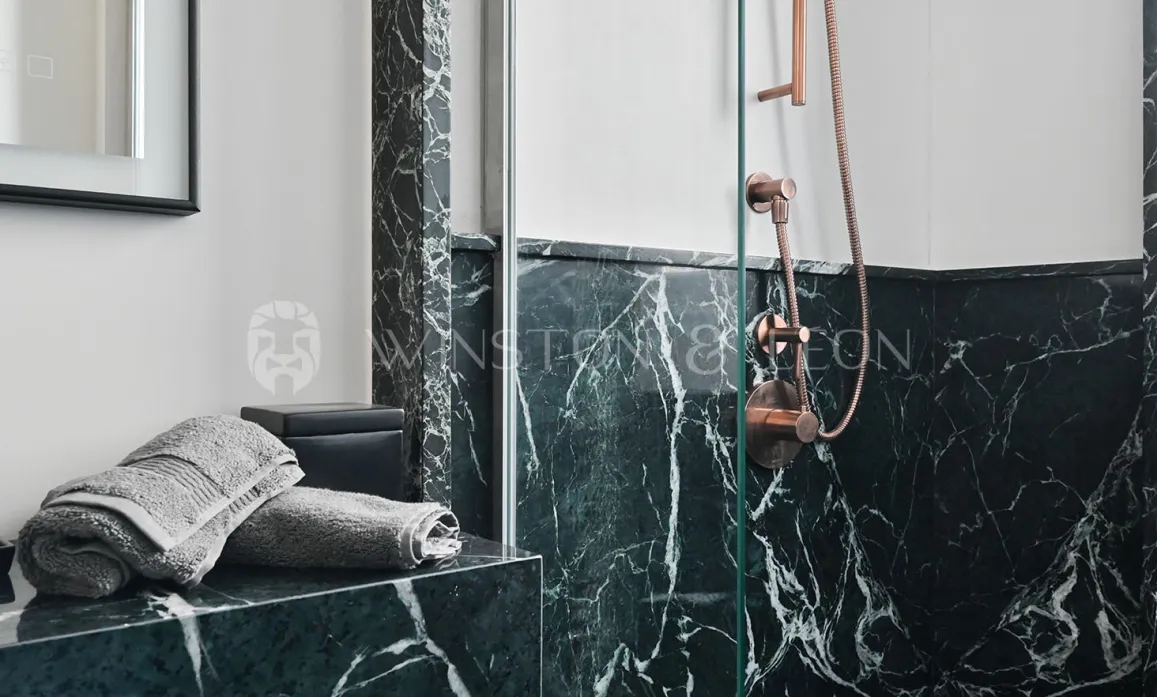 Salle de bain de luxe avec marbre vert veiné et robinetterie cuivre. Douche élégante, design contemporain. Idéal pour immobilier haut de gamme.
