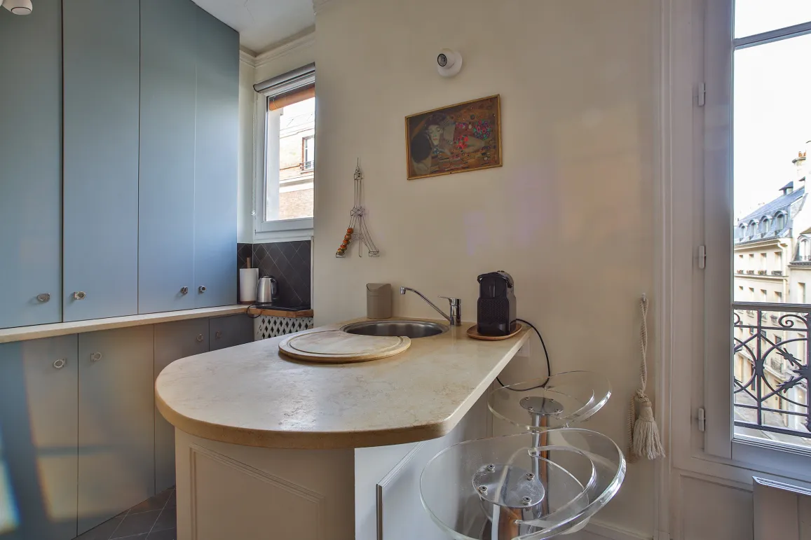 Cuisine moderne et élégante avec îlot/bar, vue imprenable sur les toits de Paris. Appartement de luxe parisien, design contemporain.