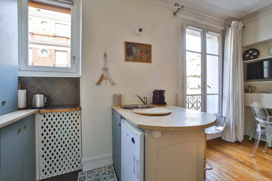 Photo d'un studio parisien optimisé avec cuisine intégrée, fenêtre lumineuse, parquet et décor Tour Eiffel. Ambiance chic et fonctionnelle.