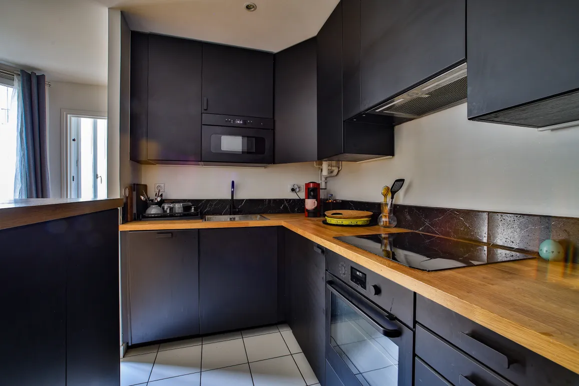 Cuisine haut de gamme, mobilier noir mat, plan de travail bois. Électroménager intégré. Ambiance moderne et luxueuse.
