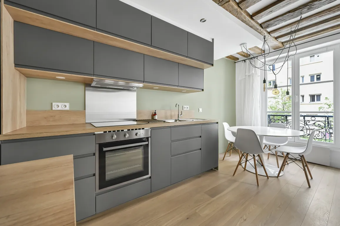 Cuisine moderne gris anthracite et bois clair. Design épuré, poutres apparentes, vue ville. Appartement de luxe lumineux.