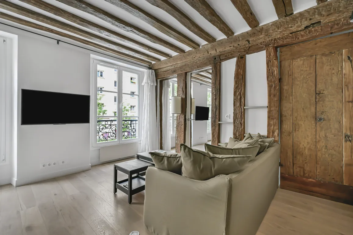 Salon lumineux d'appartement de luxe parisien avec poutres apparentes, parquet clair et touches modernes. Charme et élégance.