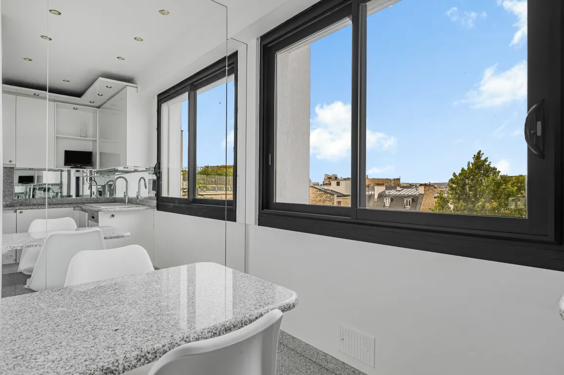 Cuisine moderne lumineuse, îlot en granit, vue urbaine. Design épuré pour un appartement de luxe contemporain.