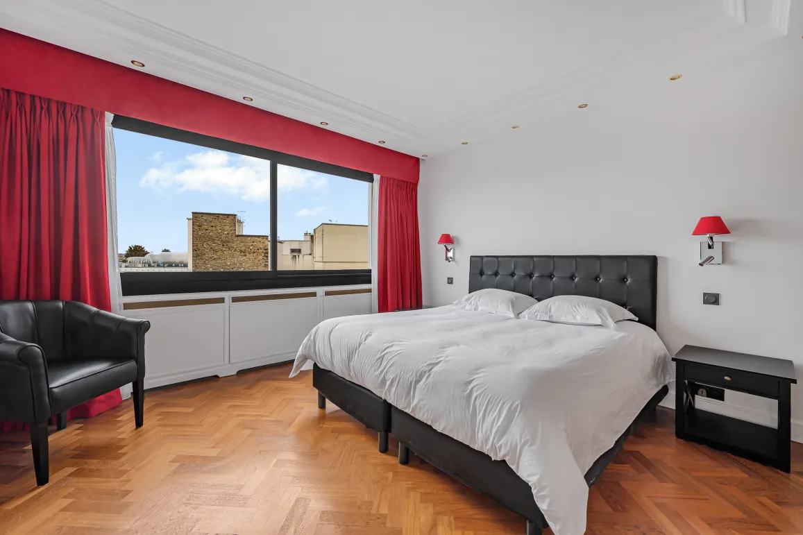 Chambre de luxe lumineuse, vue ville, parquet chevrons. Lit double élégant, fauteuil. Parfait pour immobilier haut de gamme.