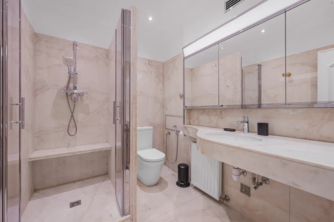 Salle de bain de luxe en marbre. Douche à l'italienne avec banc, WC design, double vasque. Élégance et confort haut de gamme.