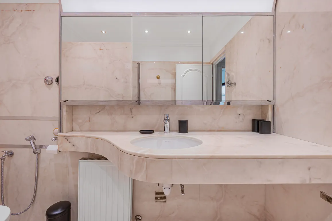 Salle de bain luxueuse en marbre clair, lavabo design et miroir. Ambiance raffinée pour une propriété d'exception.