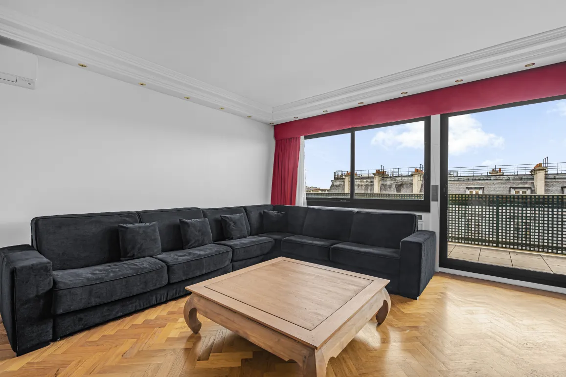 Salon moderne et lumineux d'un appartement de luxe. Grand canapé, parquet, vue sur les toits de Paris et balcon.