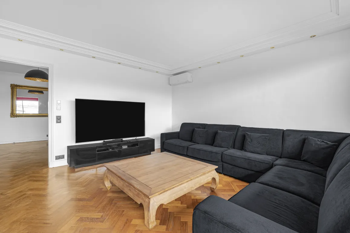 Salon de luxe moderne avec grand canapé d'angle, TV, parquet chevron. Confort et élégance pour votre intérieur.
