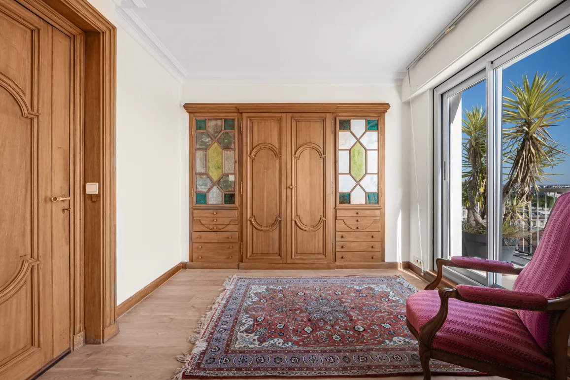 Élégant dressing en bois sur mesure avec vitraux, parquet et tapis oriental. Accès terrasse lumineuse. Ambiance chic et chaleureuse.