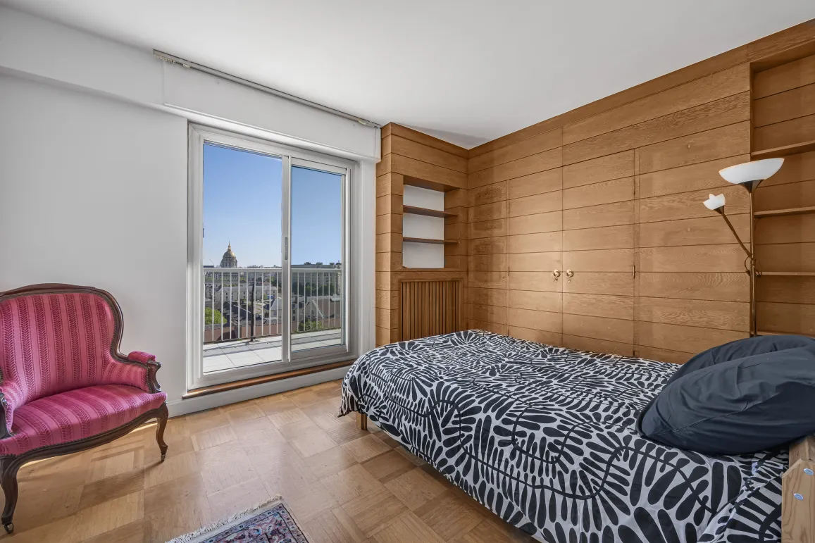 Chambre élégante avec boiseries, parquet, et balcon offrant une vue imprenable sur le dôme de la ville. Luxe et sérénité au cœur de l'appartement.