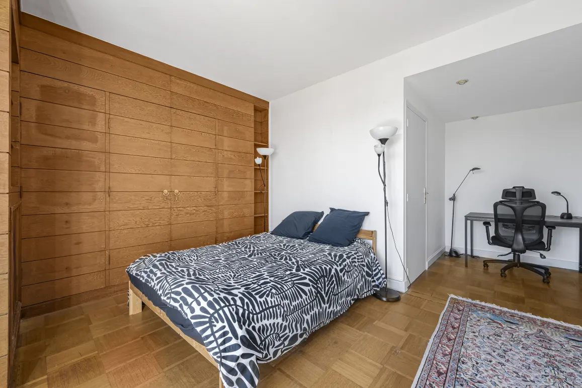 Chambre élégante avec grand rangement intégré en bois, parquet, et espace bureau discret. Confort et style pour un intérieur de luxe.