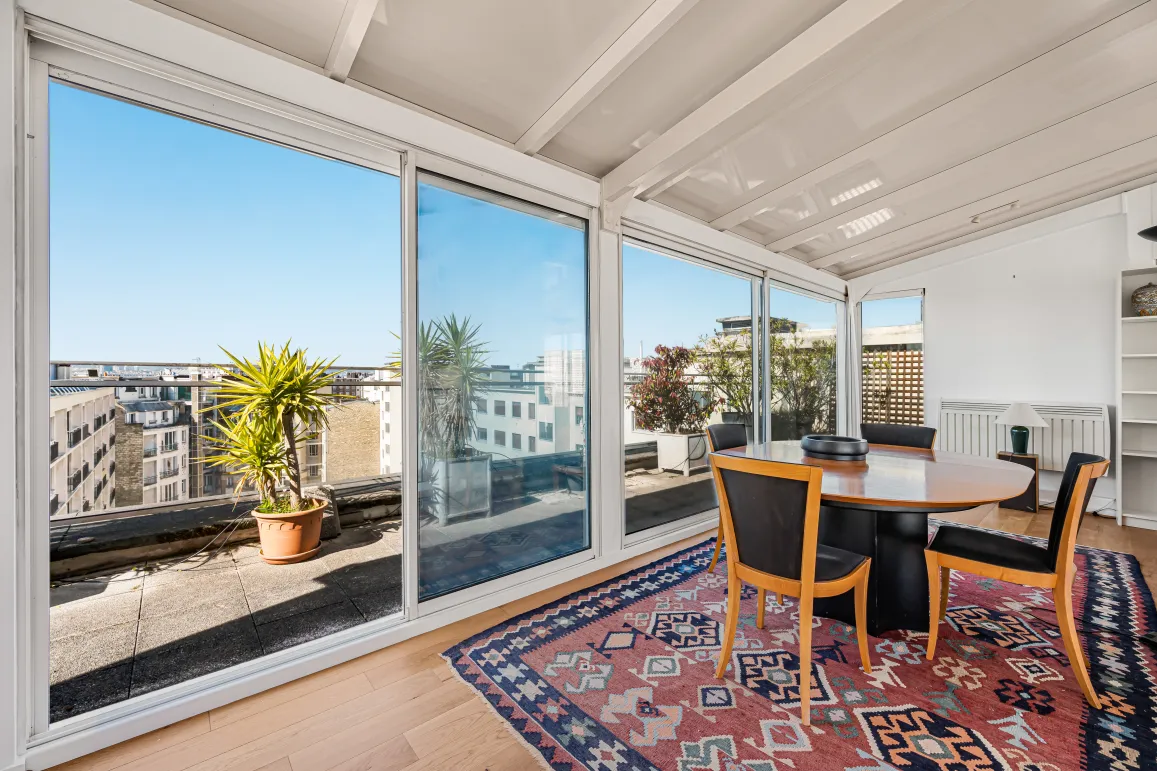 Salle à manger lumineuse avec vue panoramique sur la ville et accès terrasse. Un espace de vie urbain élégant et ensoleillé.