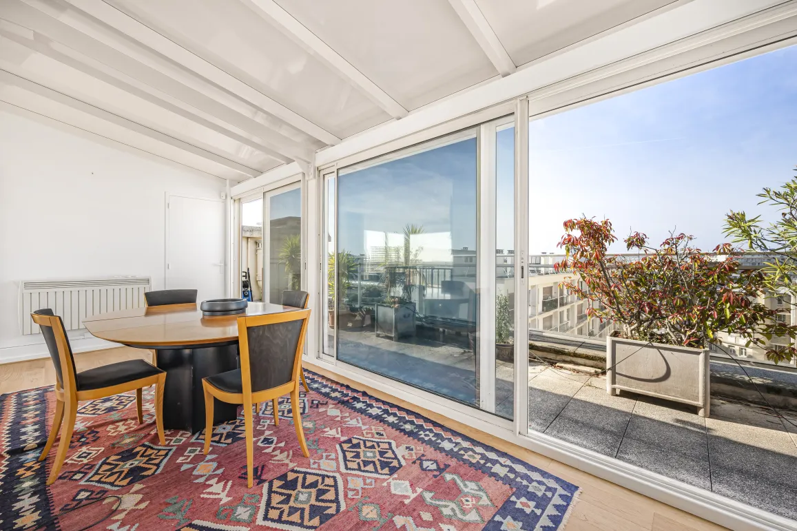 Lumineuse véranda/solarium avec salle à manger, accès direct à une terrasse privée offrant une vue dégagée sur la ville. Idéal pour un penthouse de luxe.