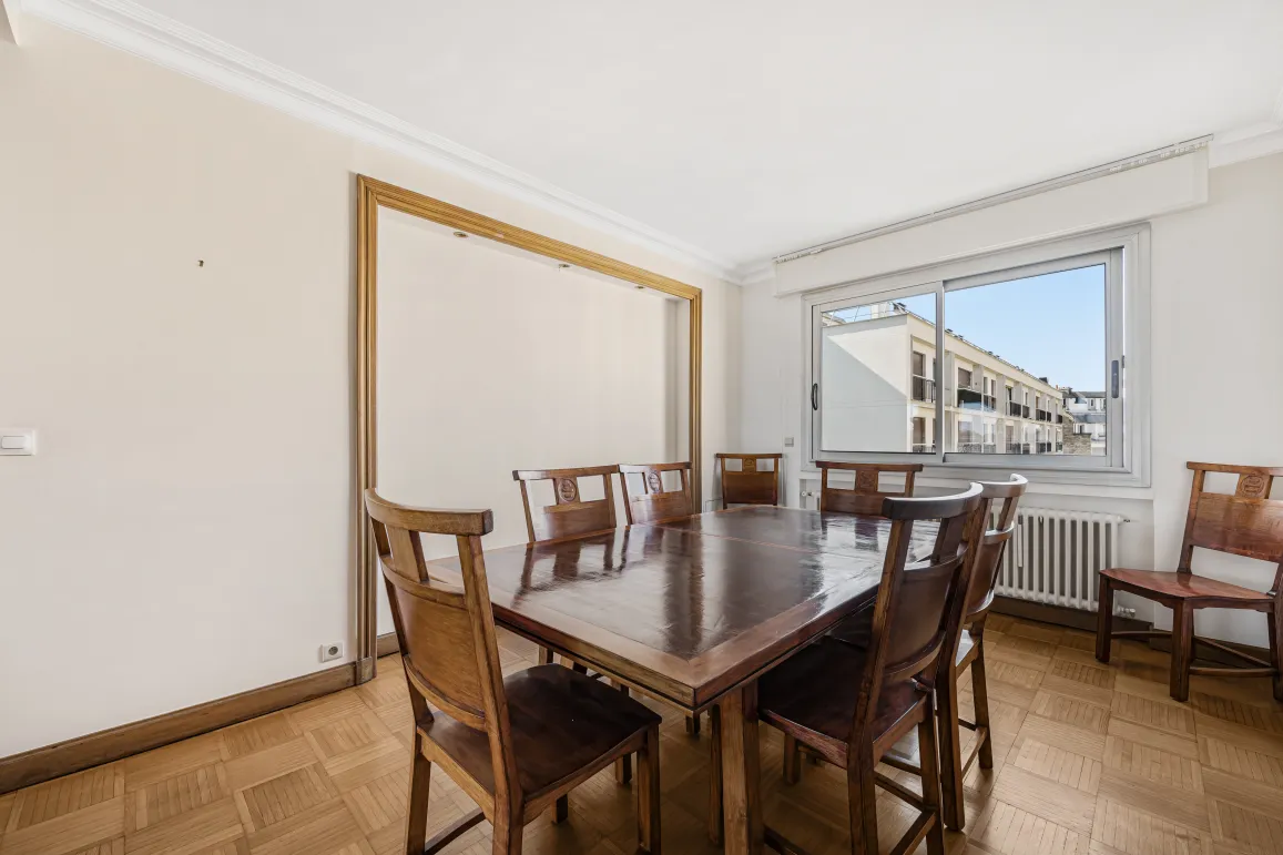 Salle à manger spacieuse et lumineuse avec parquet, grande table en bois massif et vue urbaine. Idéal pour un appartement de luxe.