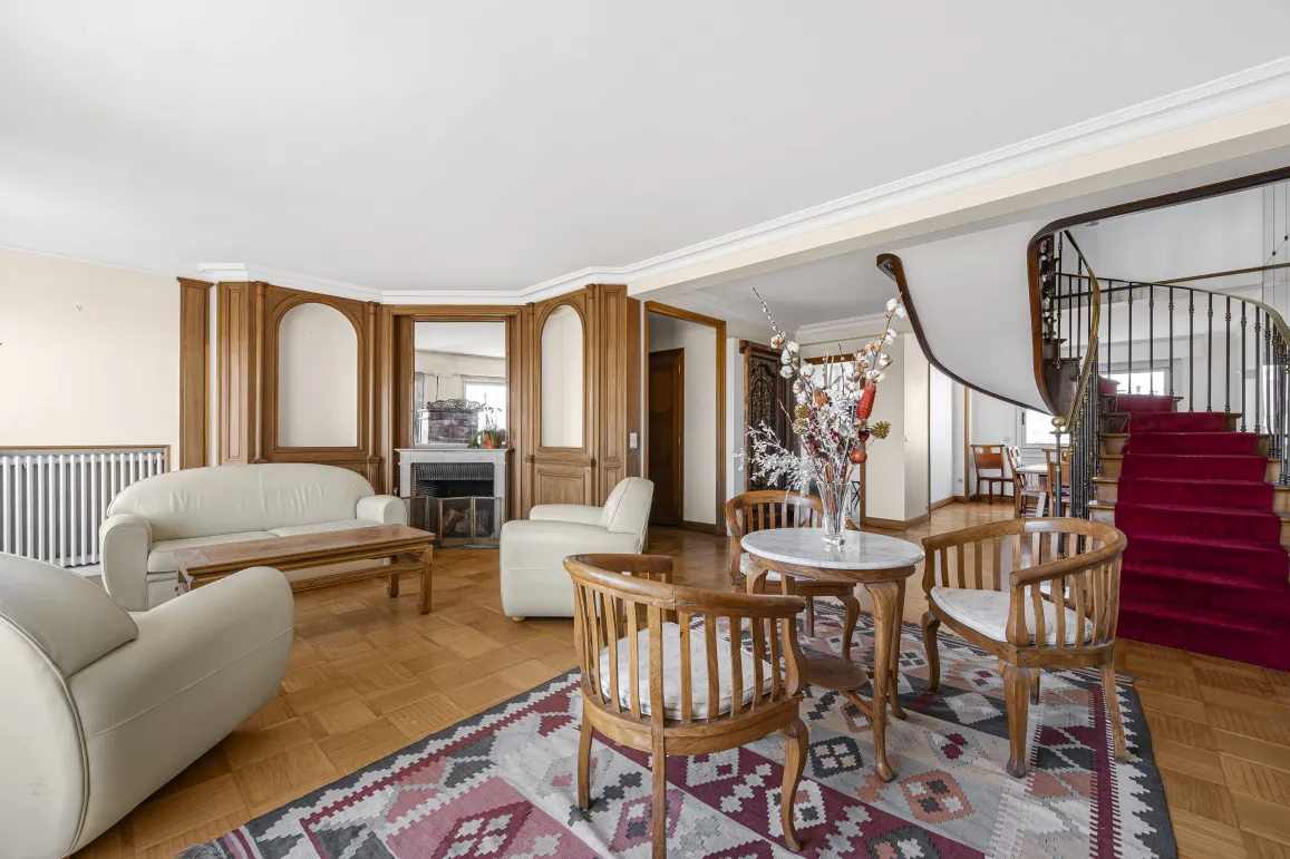 Salon de luxe élégant avec cheminée, boiseries, parquet et majestueux escalier en colimaçon. Propriété spacieuse.