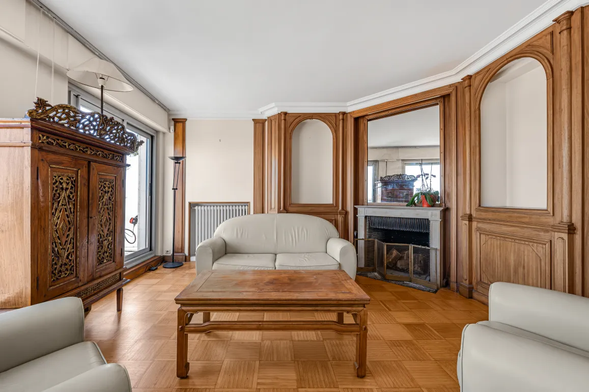 Salon de luxe avec boiseries murales, parquet, cheminée et mobilier classique. Une élégance intemporelle pour un appartement d'exception.