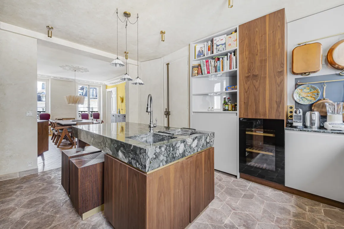 Cuisine de luxe avec îlot central en marbre et bois, design moderne et élégant. Espace ouvert sur salle à manger. Appartement haussmannien.