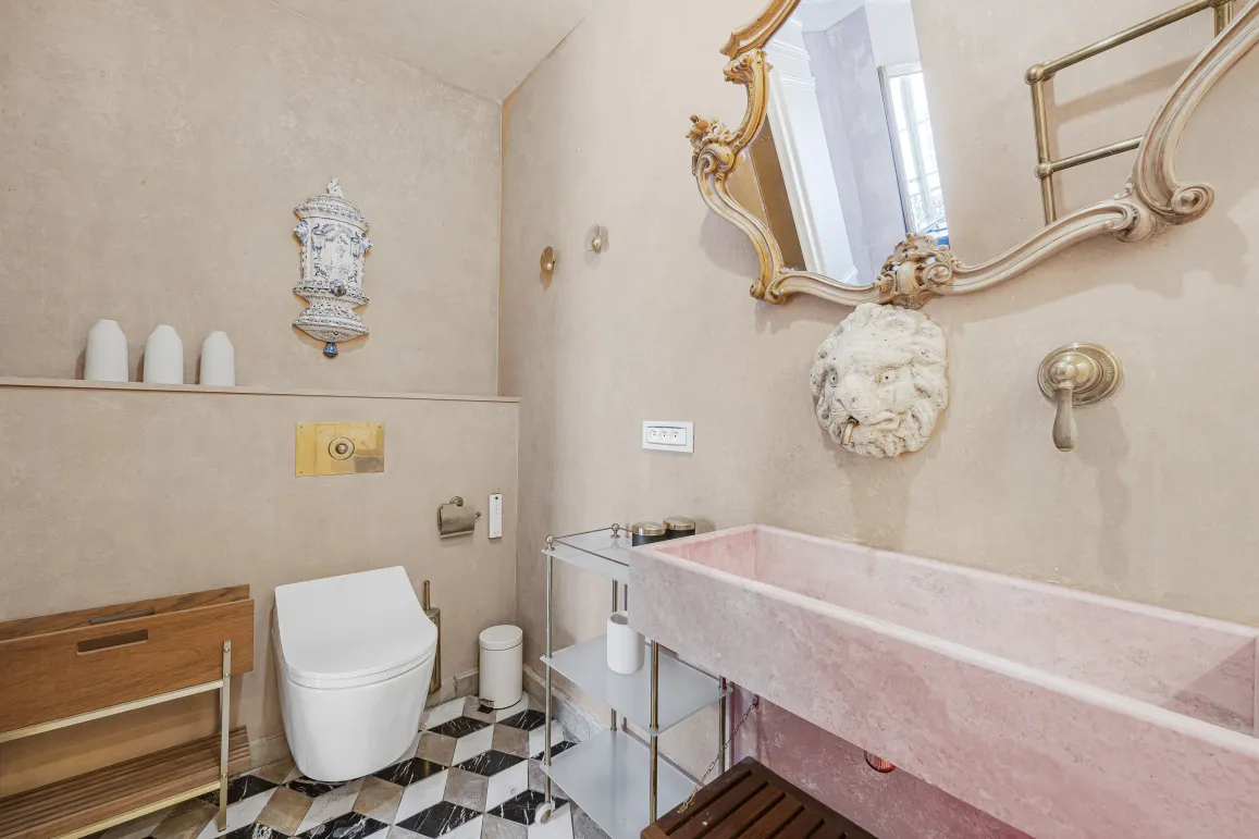 Salle de bain luxe avec lavabo marbre rose, miroir doré, toilettes design et carrelage géométrique. Ambiance élégante et raffinée.
