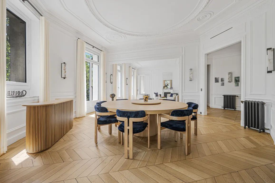 Salle à manger de luxe lumineuse, design élégant. Appartement parisien avec parquet chevrons, moulures. Raffinement et espace.