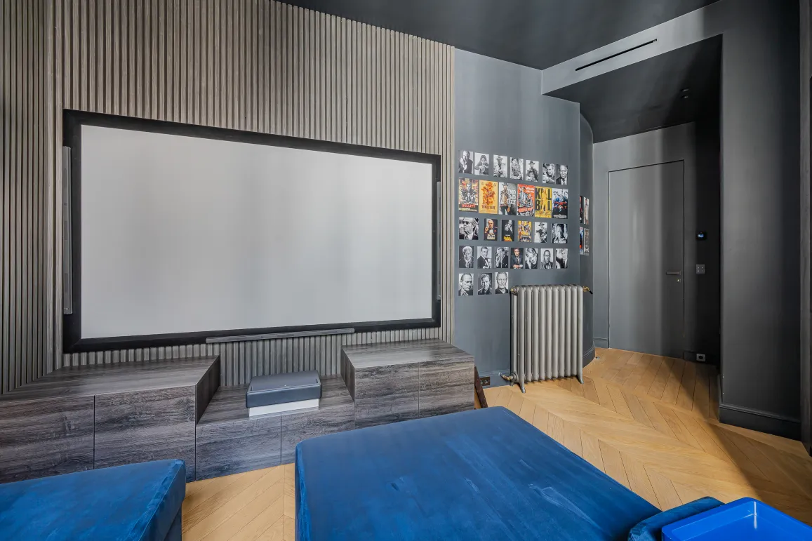 Salle de cinéma privée de luxe au design moderne. Écran géant, boiseries élégantes, parquet chevrons. Expérience immersive haut de gamme.
