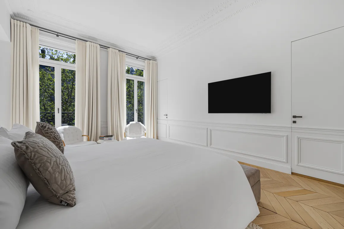 Chambre de luxe moderne, lumineuse. Grandes fenêtres, parquet chevron, TV murale. Design élégant et épuré pour un espace serein et confortable.