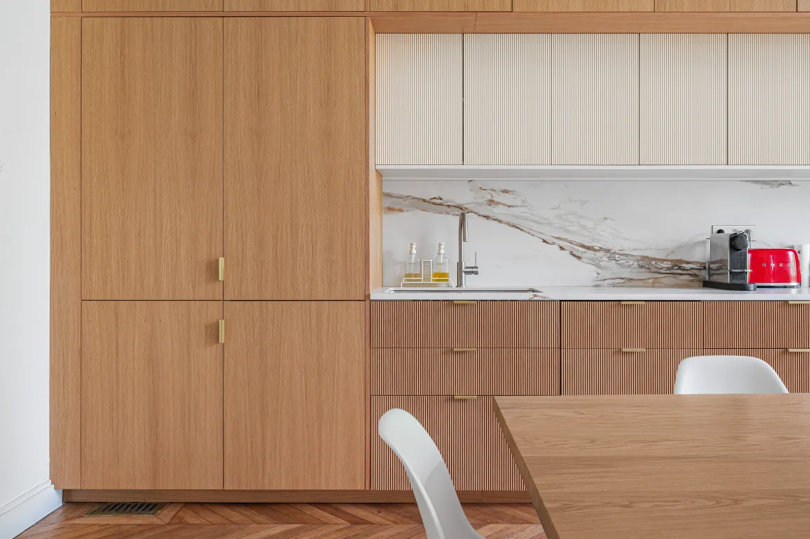 Cuisine design luxe: bois clair, marbre veiné, finitions dorées. Aménagement contemporain avec parquet chevrons et électroménager Smeg.
