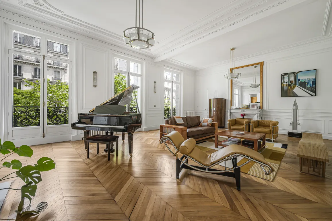 Luxe parisien: salon élégant avec grand piano, parquet chevrons, moulures et vue verdoyante. Design intemporel.