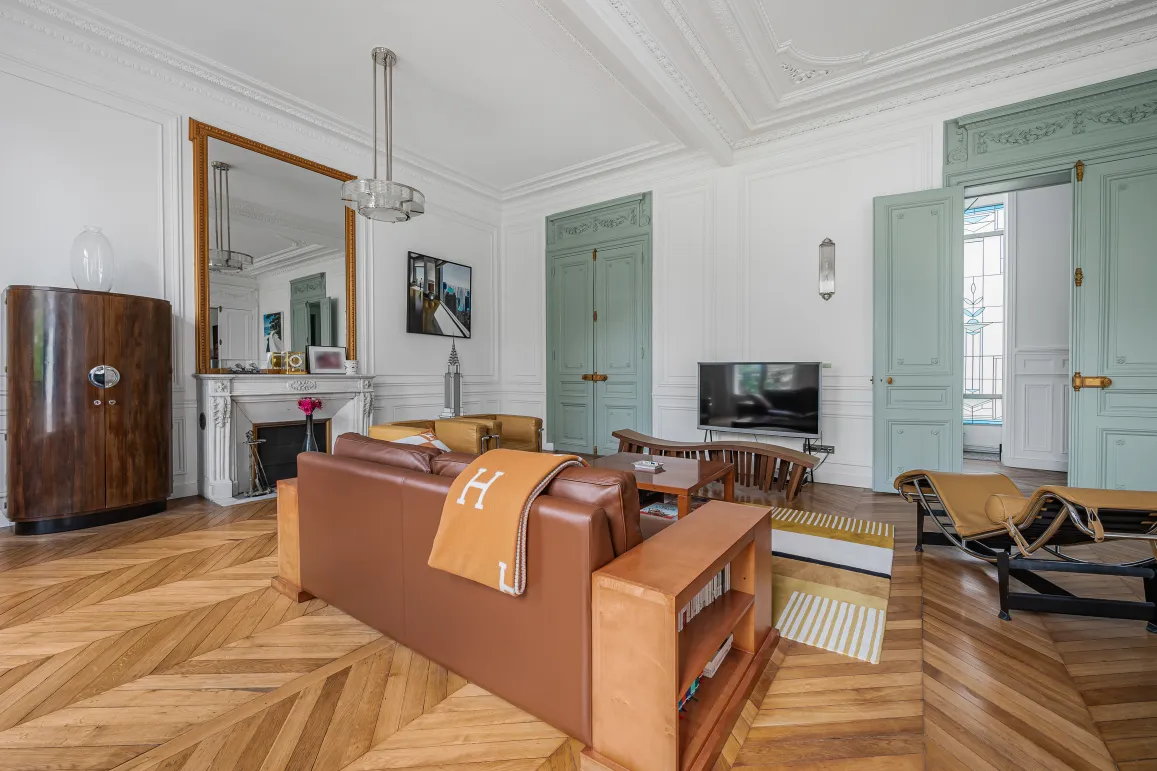 Appartement Haussmannien luxueux, salon lumineux avec parquet chevron, moulures, cheminée et mobilier design Art Déco.
