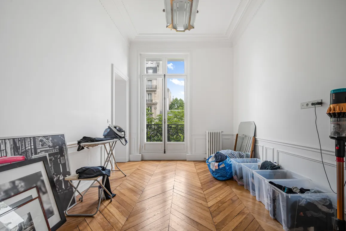 Appartement haussmannien Paris. Pièce lumineuse, parquet chevrons, moulures, fenêtre balcon. Potentiel luxe, vue verdoyante.
