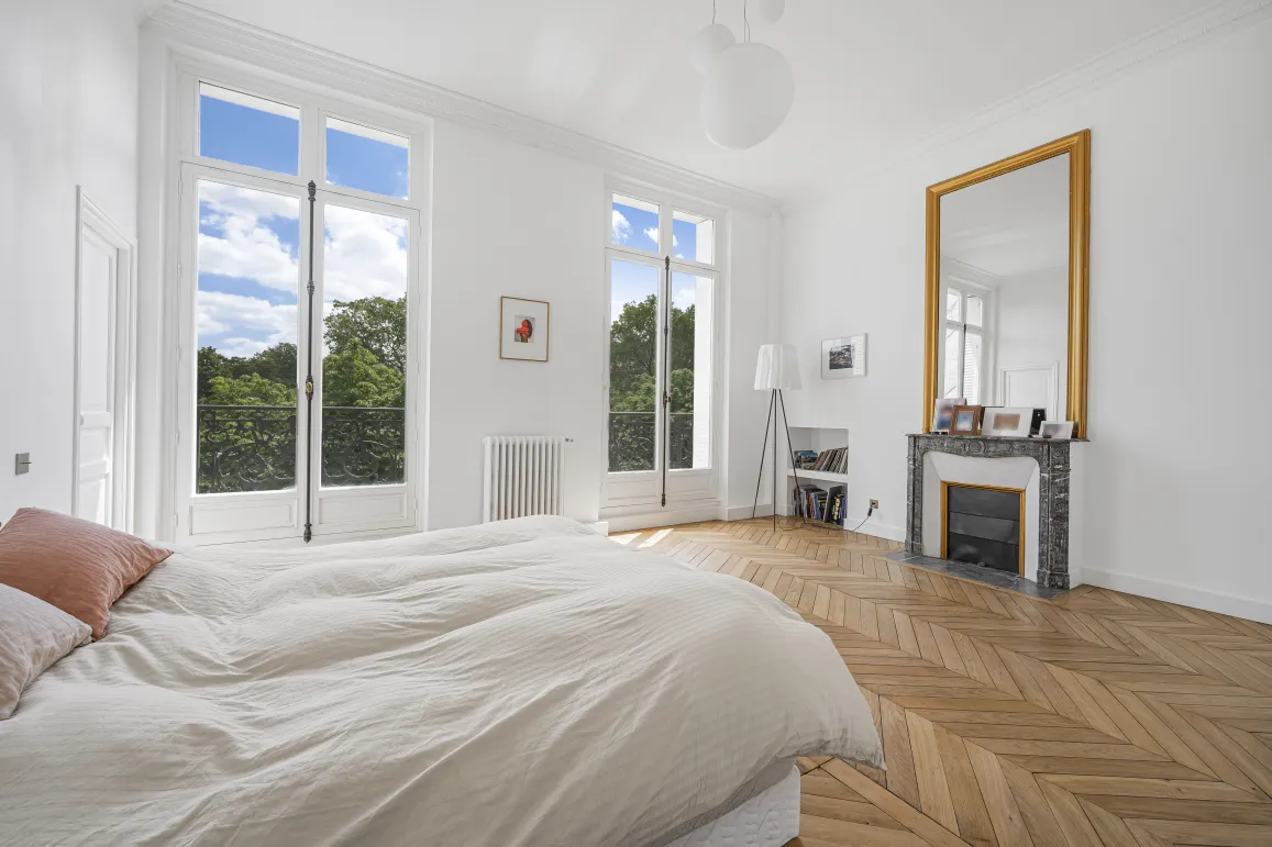 Chambre luxueuse et lumineuse avec vue imprenable sur la verdure. Parquet chevrons, cheminée et miroir doré. Élégance et confort.