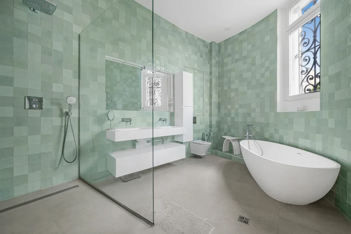 Salle de bain de luxe avec carrelage zellige vert d'eau, baignoire îlot contemporaine, douche à l'italienne et double vasque flottante.