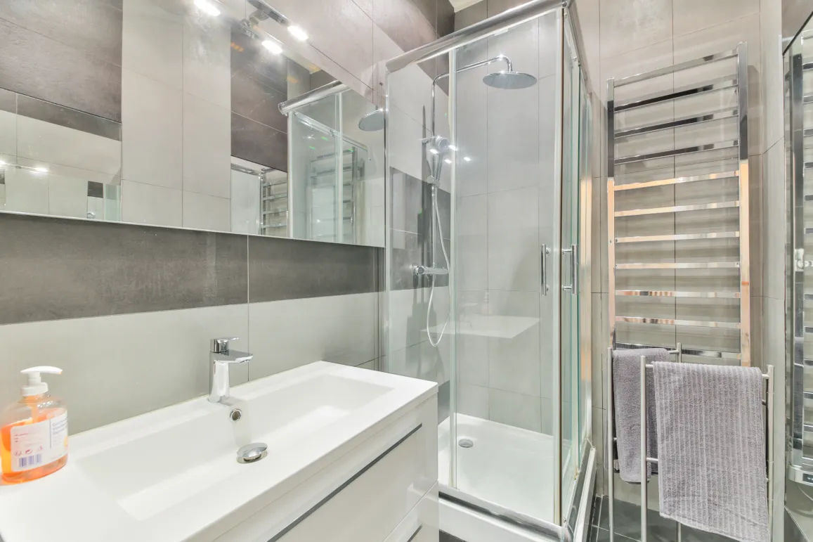 Salle de bain moderne et élégante avec douche vitrée, vasque design et sèche-serviettes chromé. Finitions haut de gamme pour un confort optimal.