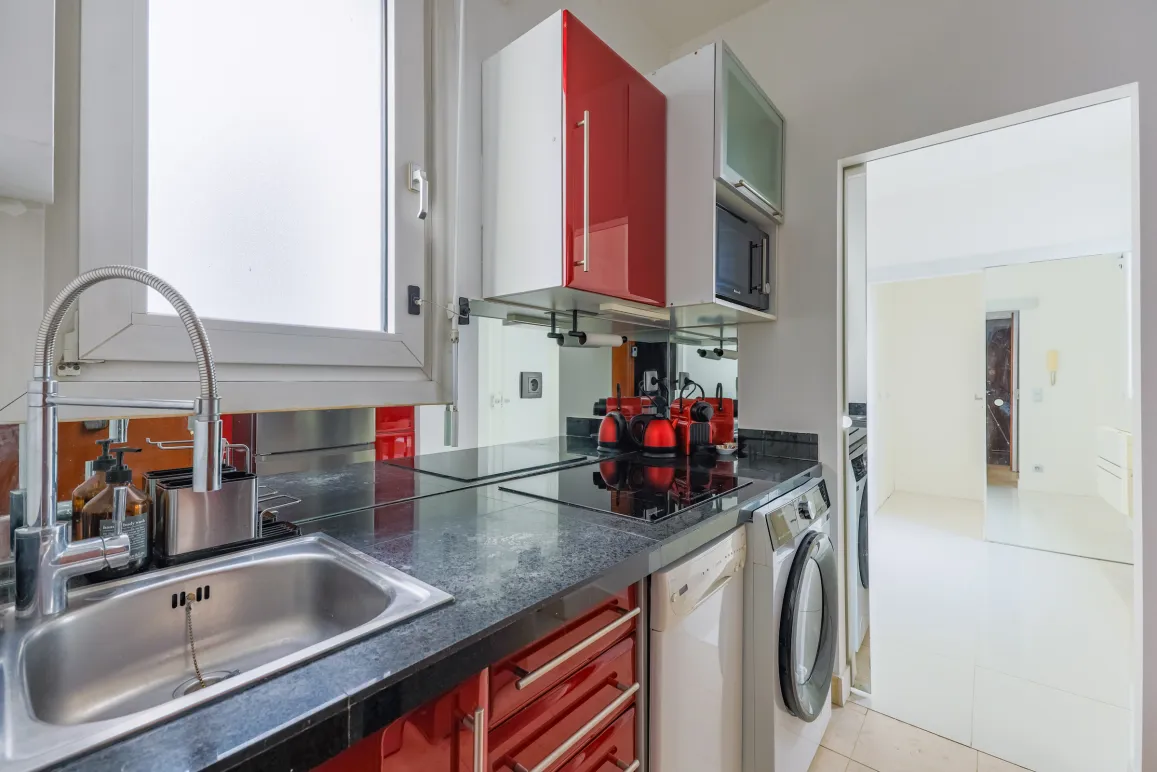 Cuisine design compacte, placards rouges brillants, plan de travail granit. Électroménager intégré. Parfait pour appartement urbain moderne.
