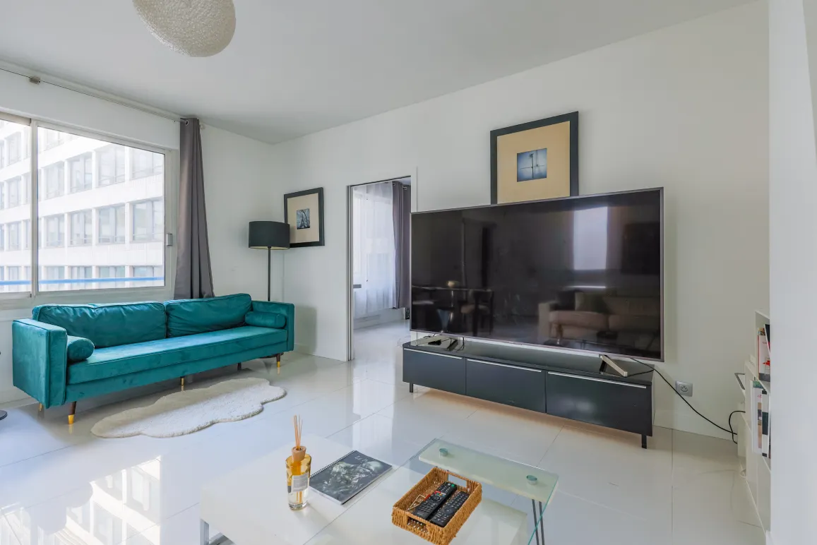 Salon moderne et lumineux avec canapé velours bleu canard, grand écran TV, design épuré. Idéal pour un appartement de luxe urbain. Confort et style.