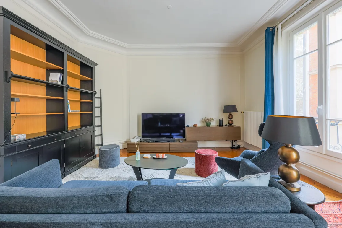 Salon parisien élégant et lumineux avec bibliothèque intégrée, canapé design et TV. Idéal pour un appartement de luxe.