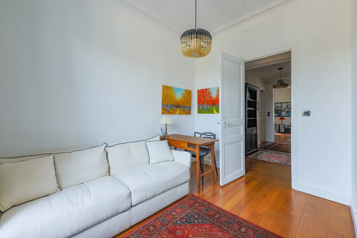 Espace de vie lumineux et raffiné: canapé design, bureau élégant, parquet chaleureux, œuvres d'art vibrantes. Idéal pour un intérieur de prestige.