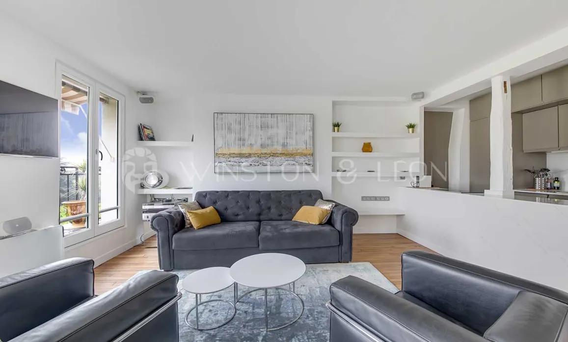 Salon moderne et lumineux d'un appartement de luxe avec canapé gris, balcon et cuisine ouverte. Design contemporain et épuré.