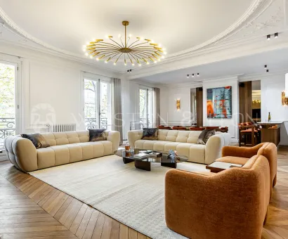 Grand salon de luxe haussmannien. Design contemporain, parquet chevrons, moulures élégantes et lustre moderne. Appartement de prestige.