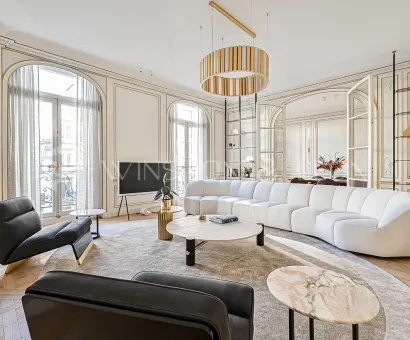 Salon Haussmannien parisien d'exception: moulures dorées, parquet point de Hongrie, canapé design blanc, mobilier luxe et lumière naturelle.