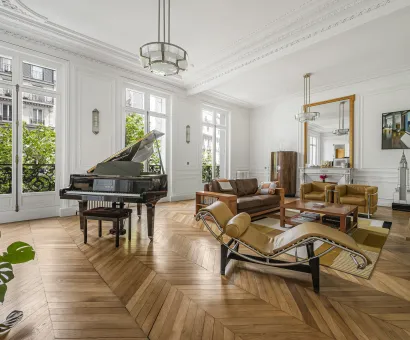 Luxe parisien: salon élégant avec grand piano, parquet chevrons, moulures et vue verdoyante. Design intemporel.