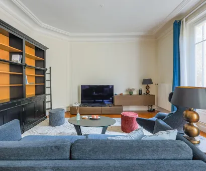 Salon parisien élégant et lumineux avec bibliothèque intégrée, canapé design et TV. Idéal pour un appartement de luxe.
