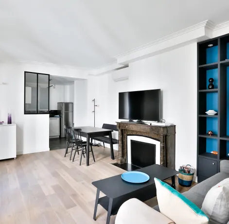 Salon moderne lumineux avec cuisine ouverte, cheminée, rangements intégrés bleus. Design contemporain pour appartement de luxe.