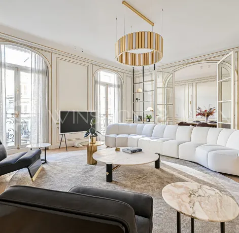 Salon Haussmannien parisien d'exception: moulures dorées, parquet point de Hongrie, canapé design blanc, mobilier luxe et lumière naturelle.