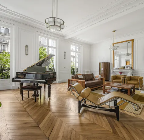 Luxe parisien: salon élégant avec grand piano, parquet chevrons, moulures et vue verdoyante. Design intemporel.