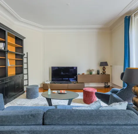 Salon parisien élégant et lumineux avec bibliothèque intégrée, canapé design et TV. Idéal pour un appartement de luxe.