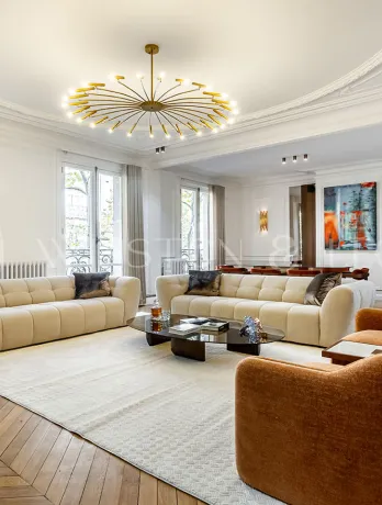 Grand salon de luxe haussmannien. Design contemporain, parquet chevrons, moulures élégantes et lustre moderne. Appartement de prestige.