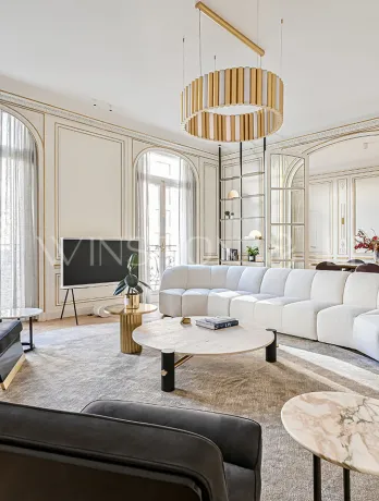 Salon Haussmannien parisien d'exception: moulures dorées, parquet point de Hongrie, canapé design blanc, mobilier luxe et lumière naturelle.