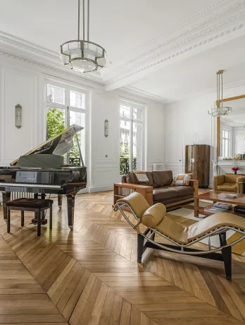 Luxe parisien: salon élégant avec grand piano, parquet chevrons, moulures et vue verdoyante. Design intemporel.