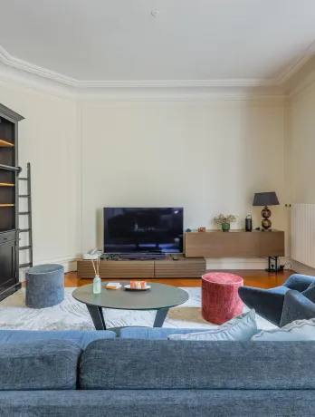 Salon parisien élégant et lumineux avec bibliothèque intégrée, canapé design et TV. Idéal pour un appartement de luxe.